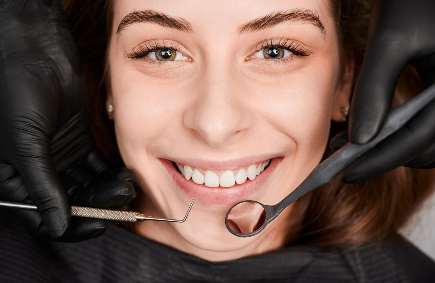 Paciente jovem sorrindo em consulta com dentista utilizando luvas pretas e espelho clínico no Jardim Anália Franco.