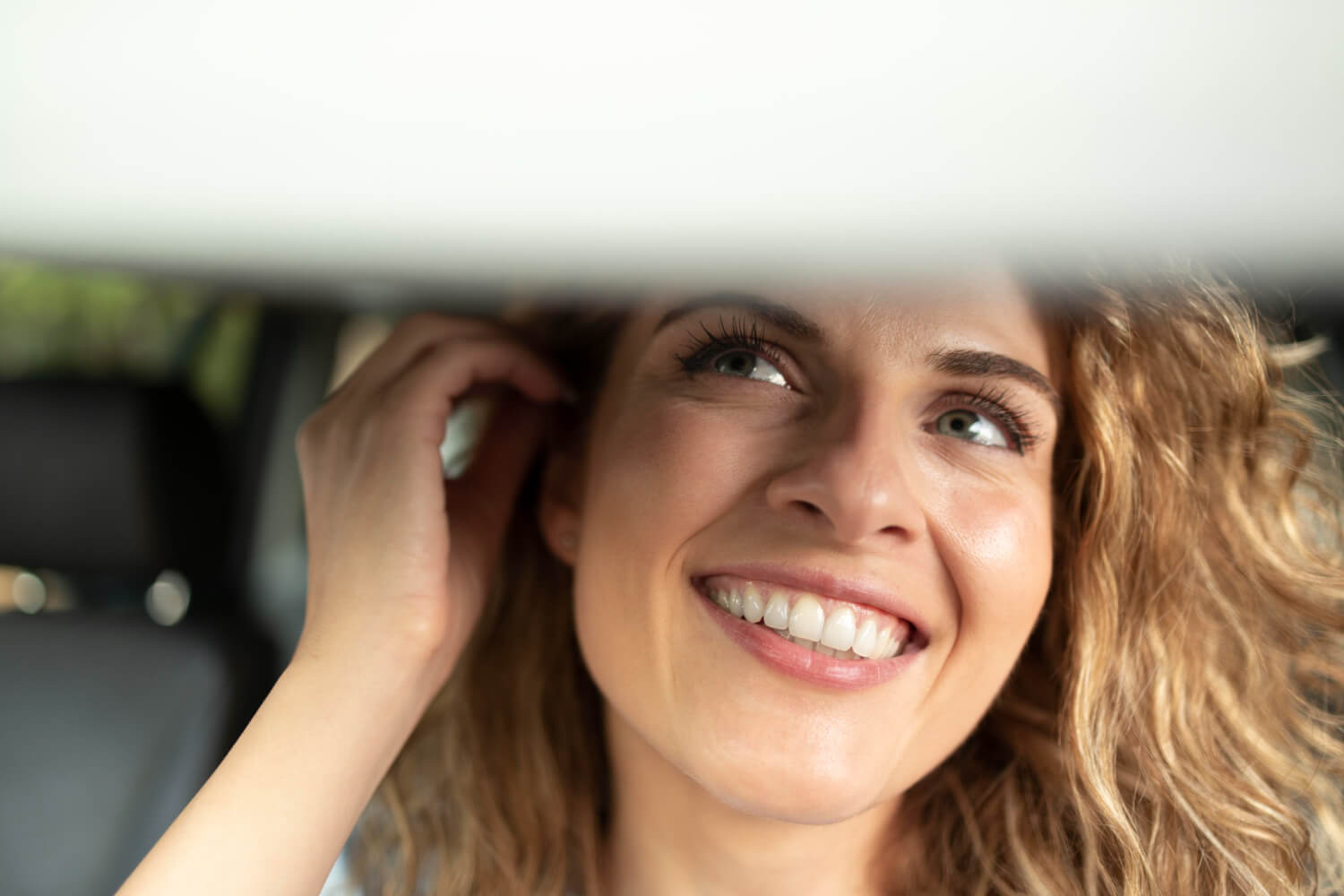Mulher sorri no espelho do carro, destacando a durabilidade das lentes de porcelana na Clínica Arte Dental no Jd Anália Franco.