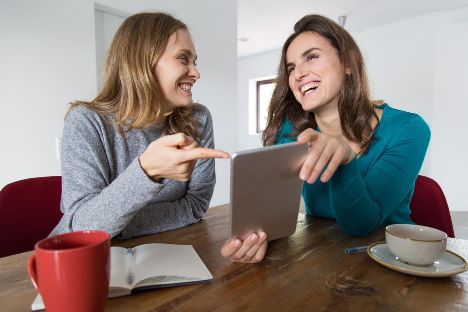 Duas amigas sorrindo e conversando com um tablet. Entenda como funciona a adaptação da fala com Invisalign no Jardim Anália Franco.