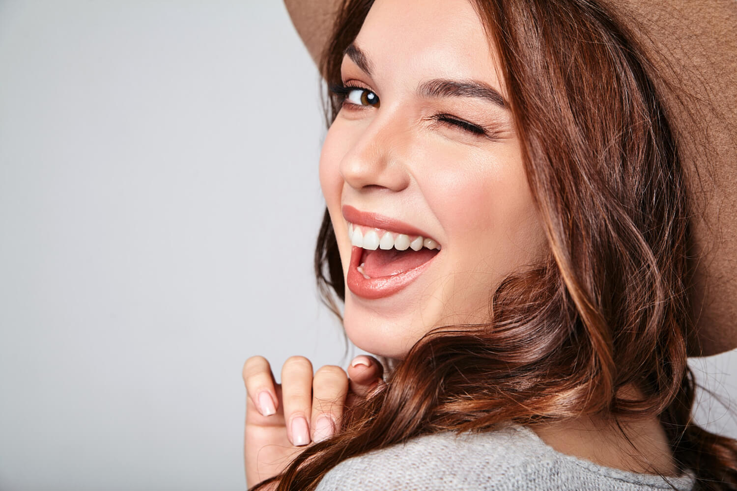 Mulher sorridente com dentes alinhados piscando. Tratamento com Invisalign no Jardim Anália Franco pela Clínica Arte Dental.